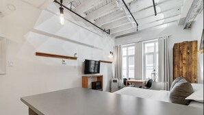 A modern living room with a large gray sofa, a TV, and a dining area with a table and chairs. - INITIAL | MEMORY FACTORY | Centre-Ville de Québec (Québec City)