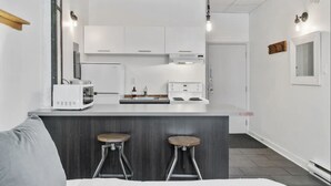 A modern kitchen with white cabinets, a central island with stools, and a built-in oven. - INITIAL | MEMORY FACTORY | Centre-Ville de Québec (Québec City)