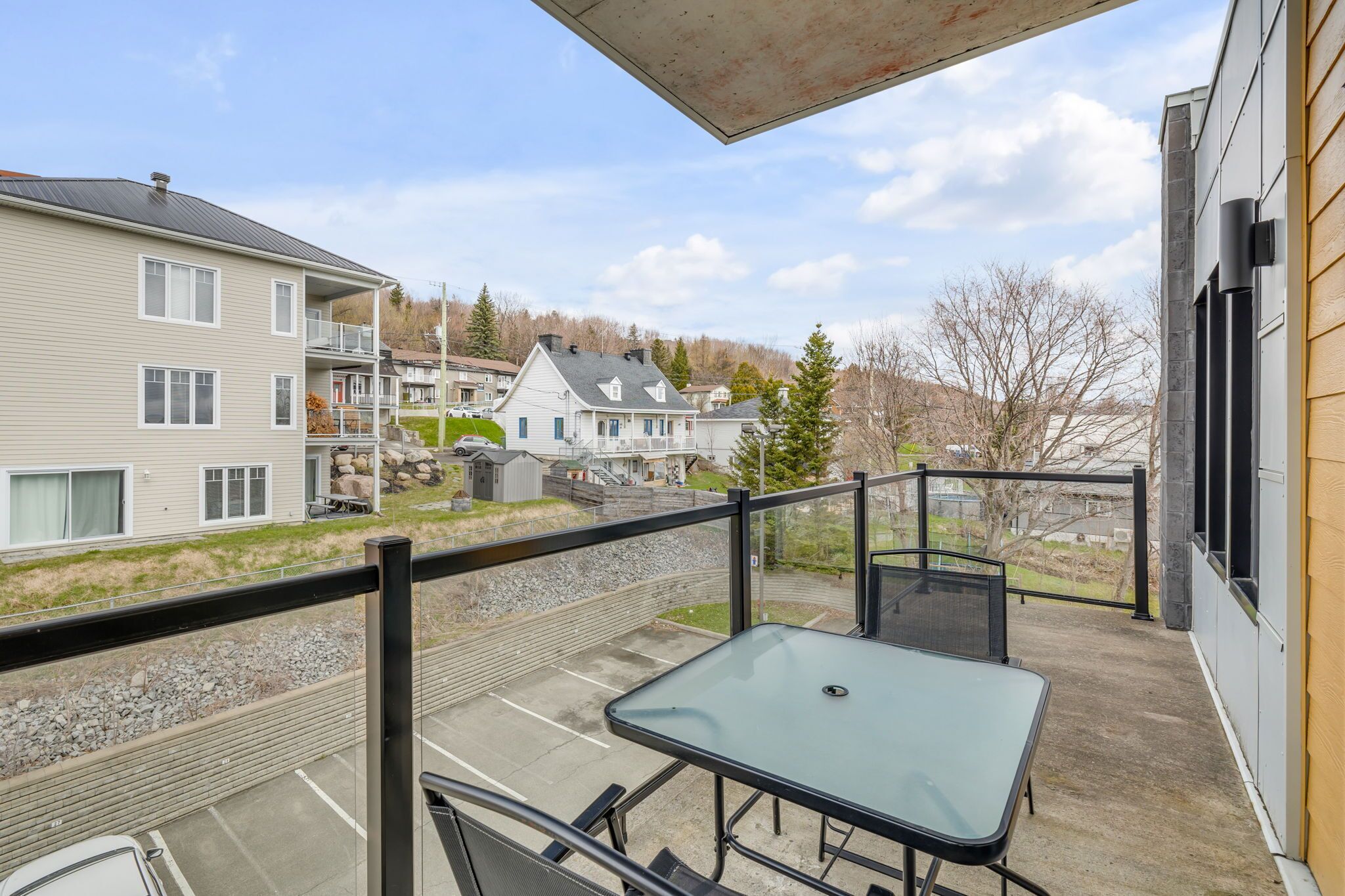 A balcony with a table and chairs, overlooking a parking area and residential buildings.