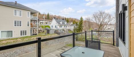 A balcony with a table and chairs, overlooking a parking area and residential buildings.