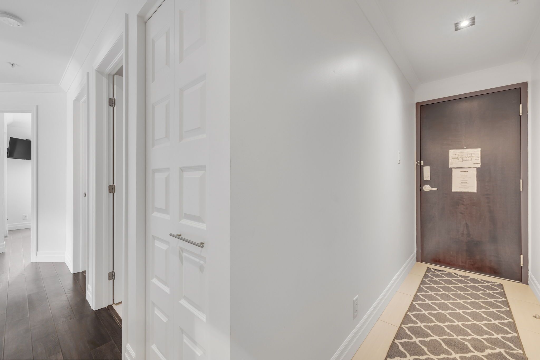 Un pasillo con puertas blancas, una puerta de madera oscura y un tapete estampado.