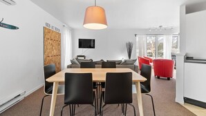 Un espace repas moderne avec une table en bois et des chaises noires, ainsi qu’une chaise rouge et un grand luminaire suspendu.