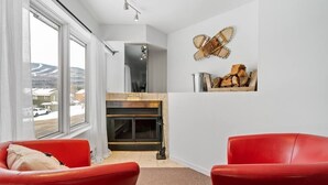 Un salon moderne avec une cheminée, des fauteuils en cuir rouge et une vue sur l’extérieur.