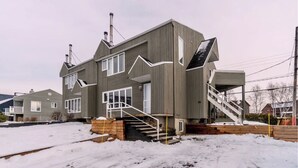 Une maison moderne à deux étages, dotée d’un toit à forte pente, d’une cheminée bien visible et d’un escalier menant à l’entrée.