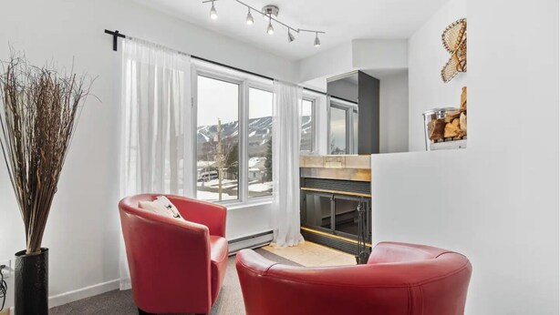 Un salon moderne avec une cheminée, des fauteuils en cuir rouge et une grande fenêtre donnant sur les montagnes.