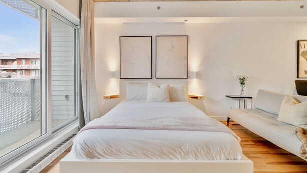 A modern bedroom with a large bed, a sofa, and a view of the city.