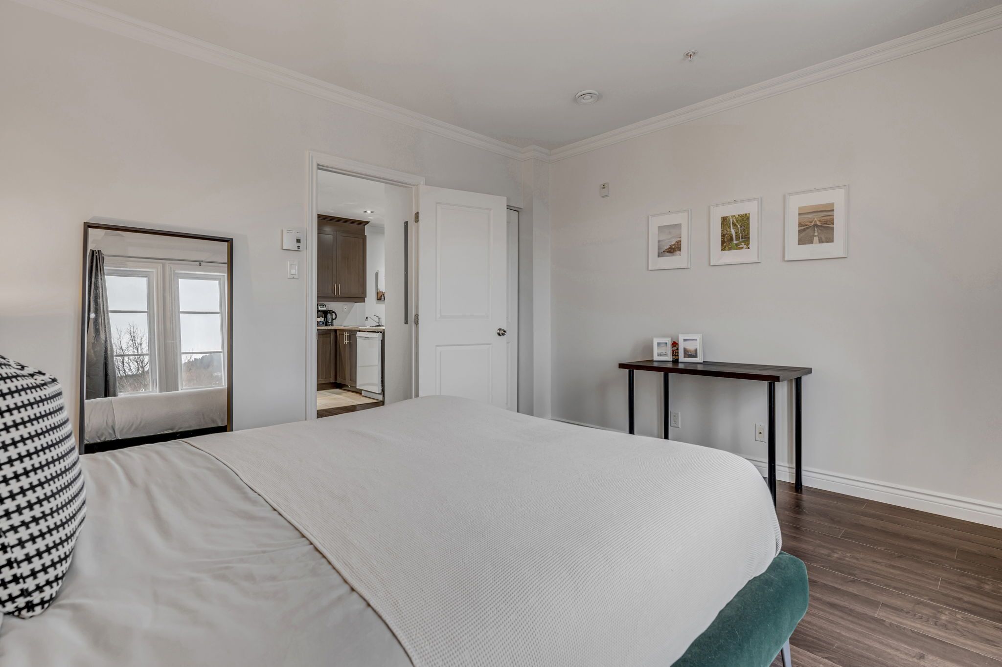 A bedroom with a large bed, a bedside table, a chair, a door leading to a bathroom, and a small table with pictures on the wall.