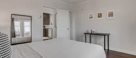 A bedroom with a large bed, a bedside table, a chair, a door leading to a bathroom, and a small table with pictures on the wall.