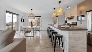 A modern kitchen with a central island, bar stools, pendant lighting, and a dining area with a table and chairs.