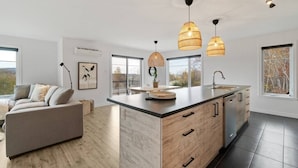 A modern kitchen with a large island, pendant lights, and a view of the outdoors.