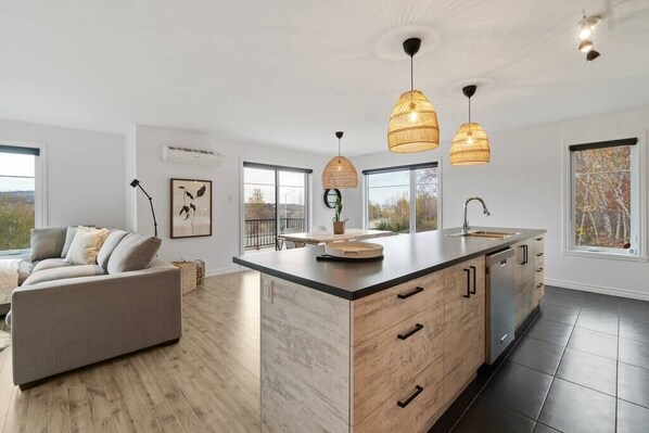 Une cuisine moderne dotée d’un grand îlot central, de luminaires suspendus et offrant une vue sur l’extérieur.