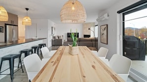 A modern kitchen with a wooden dining table, white chairs, and hanging rattan light fixtures.