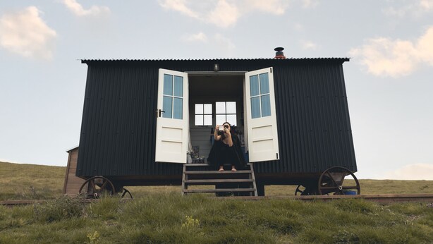 Un petit bâtiment d’un seul étage, avec une porte ouverte, situé sur une colline herbeuse sous un ciel dégagé.