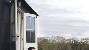 Une personne est assise sur une terrasse en bois, à l’extérieur d’un bâtiment doté d’une porte et de fenêtres.