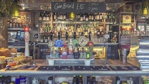 Un espace bar avec un assortiment de bouteilles et un panneau indiquant les prix du gin.