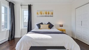 Ein Schlafzimmer mit einem großen Bett, einem Nachttisch mit Lampe, einem Fenster mit Vorhängen und einer Tür.