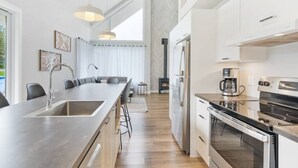 A modern kitchen with a central island, stainless steel appliances, and a large window providing natural light. - Initial | Soeur No2 | MSA (Saint-Ferréol-les-Neiges)