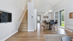 A modern kitchen with a wooden staircase, a dining area with chairs, and large windows. - Initial | Soeur No2 | MSA (Saint-Ferréol-les-Neiges)