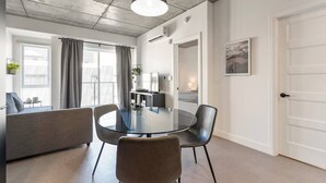 A modern living room with a glass dining table, grey sofa, and a large window with curtains.