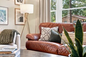 A brown leather sofa with patterned cushions, a floor lamp, and framed pictures on the wall.