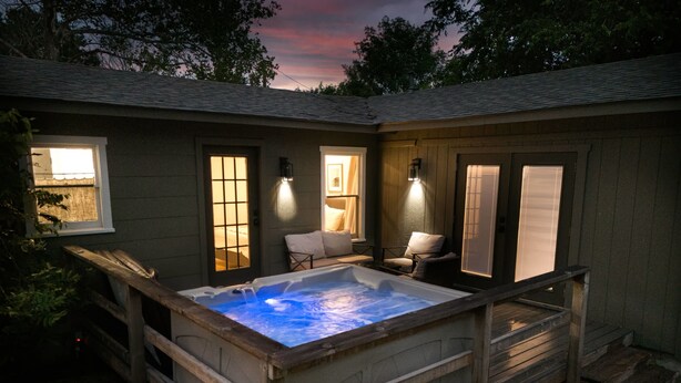 Un bain à remous avec une terrasse en bois, un espace patio avec des chaises et un coin salon couvert offrant une vue sur le ciel.