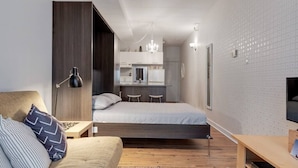 A compact studio apartment with a bed, kitchenette, and a small seating area.