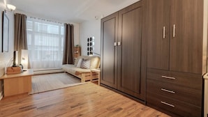 A room with a large wardrobe, a sofa, a bedside table, and a window with curtains.