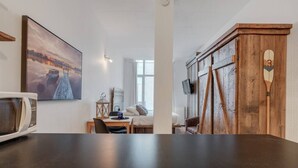 A modern room with a large window, a wooden wardrobe, a bed, a desk, and a television.