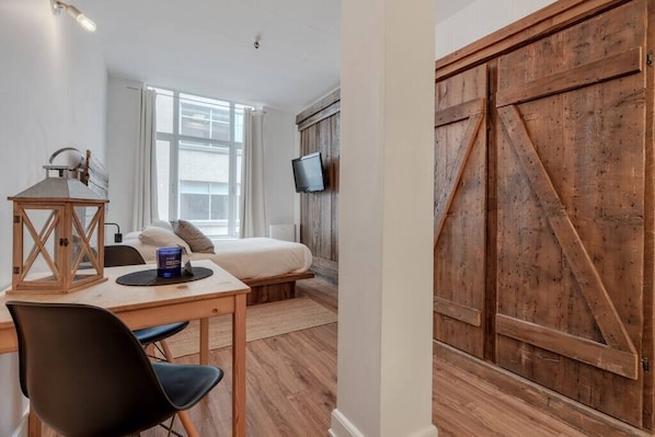 A bedroom with a bed, a desk with a chair, a TV mounted on the wall, and a wooden barn door.