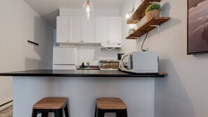 A compact kitchen with white cabinets, a black countertop, two wooden stools, and a hanging light fixture.