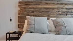 A bed with a wooden headboard, a bedside table with a lamp, and a remote control on the table.