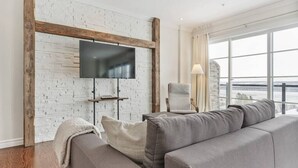 Een moderne woonkamer met een witte bakstenen muur, een wandgemonteerde televisie, een bank en uitzicht door grote ramen.