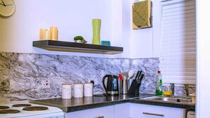 Une cuisine compacte avec des meubles blancs, une cuisinière, un four à micro-ondes et une machine à café.