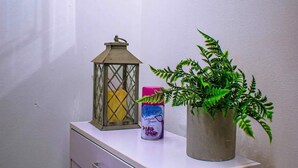Une salle de bain avec un meuble blanc, une plante en pot, un aérosol parfumé à la lavande et une lanterne.