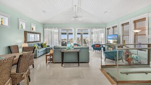 A spacious living room with a large sofa, a dining table, and a TV. - 3BR Lakefront Retreat w/ Modern Decor + Fire Pit | It Doesn't Get Any Better (Destin)
