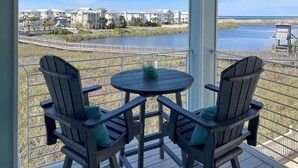 A balcony with two Adirondack chairs and a small round table, overlooking a river and a bridge with buildings in the background. - 3BR Lakefront Retreat w/ Modern Decor + Fire Pit | It Doesn't Get Any Better (Destin)