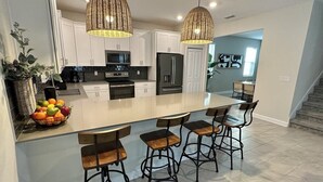 A modern kitchen with white cabinets, a large island with bar stools, and a built-in oven. - Luxury Family Estate | Orlando Pool and Game Room (Kissimmee)