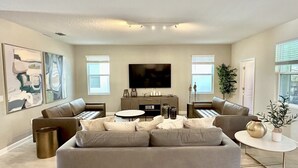 A modern living room with a large sofa, a coffee table, and a flat-screen TV mounted on the wall. - Luxury Family Estate | Orlando Pool and Game Room (Kissimmee)