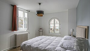 Un dormitorio con cama, un radiador, una ventana con cortinas, una lámpara colgante y vistas al exterior.
