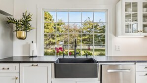 A kitchen with white cabinets, a black countertop, a stainless steel dishwasher, and a window with a view of trees and a white fence. - Minutes from Downtown St. Michaels | Pool | Hot Tub | Pickle Ball Court (Saint Michaels)