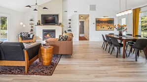 A spacious living area with a fireplace, a dining table with chairs, and a television mounted on the wall. - Minutes from Downtown St. Michaels | Pool | Hot Tub | Pickle Ball Court (Saint Michaels)
