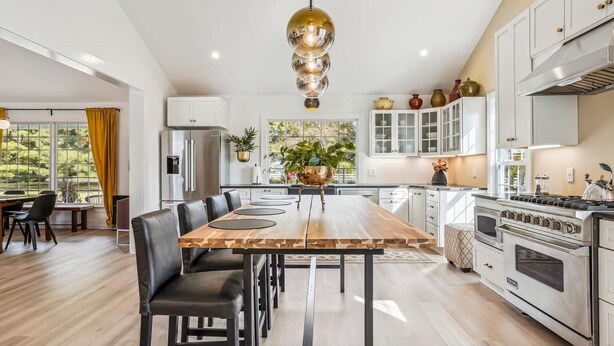 A modern kitchen with a central island, stainless steel appliances, and a dining area with a long table and chairs. - Minutes from Downtown St. Michaels | Pool | Hot Tub | Pickle Ball Court (Saint Michaels)