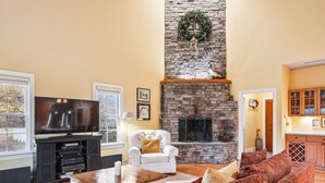 A living room with a stone fireplace, a television, a white armchair, and a patterned sofa. - Minutes from Downtown Easton and St. Michaels | Pool | 1st Floor Bedroom | Pet F (Easton)