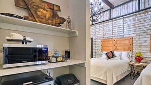 Een hotelkamer met een bed, nachtkastje en een wand met een houten hoofdeinde. Er is een plank met een magnetron, een prullenbak en een klein tafeltje met een vaas.