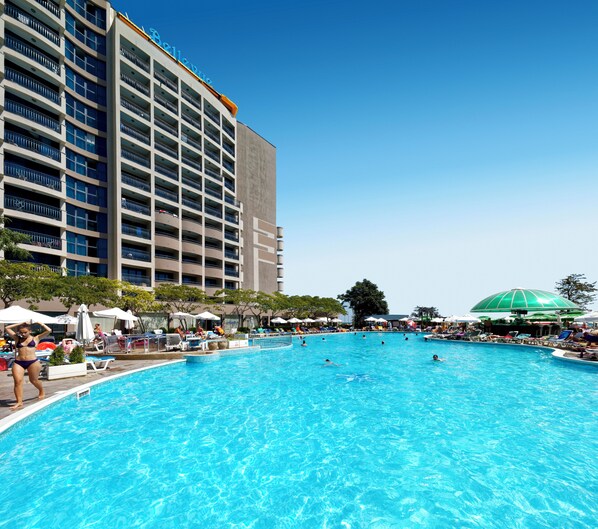 A hotel with a swimming pool, multiple balconies, and outdoor umbrellas.
