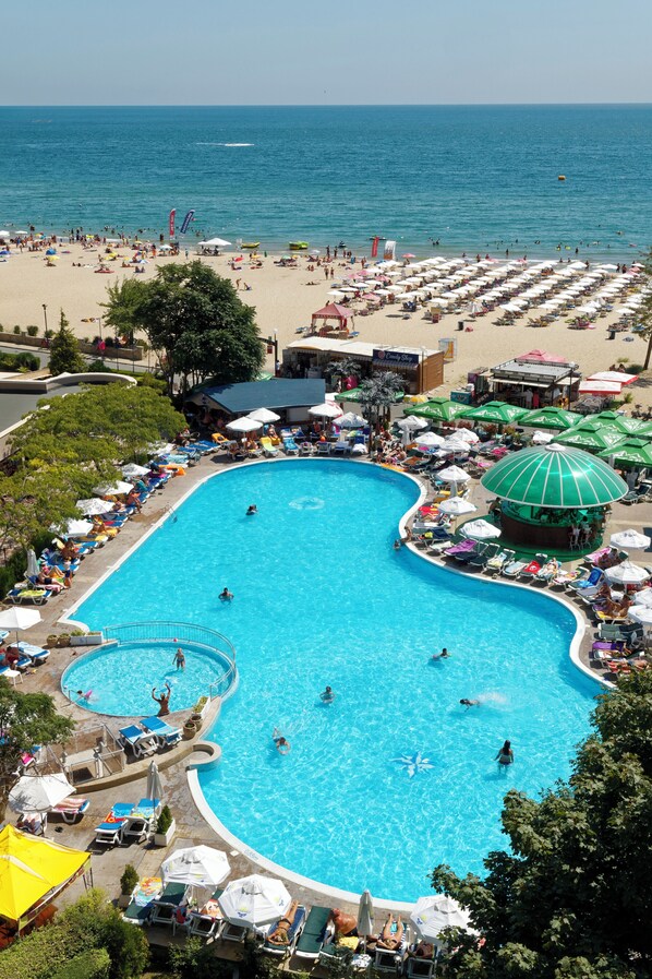A large swimming pool surrounded by beach chairs and umbrellas, with a view of the ocean.