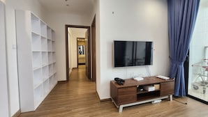 Una sala de estar moderna con un televisor de pantalla plana, suelo de madera, una estantería empotrada y un ventanal corredero con vistas.