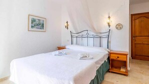 A neatly made bed with a white bedspread and a green skirt, two bedside tables with lamps, a wooden door, and a framed picture on the wall. - VILLA FELIZ, beach, pool, wifi, a/a, 10 pax (Moravit)