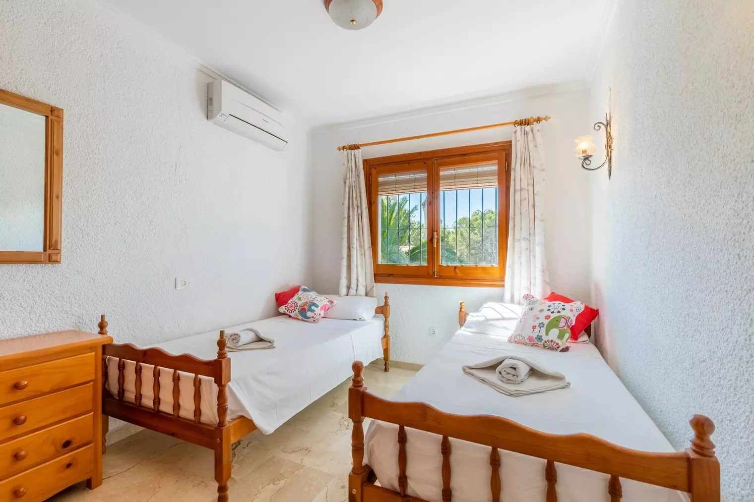 Ein Zimmer mit zwei Holzbett, einem Holzschrank, einem Fenster mit Vorhängen und einer Klimaanlage.