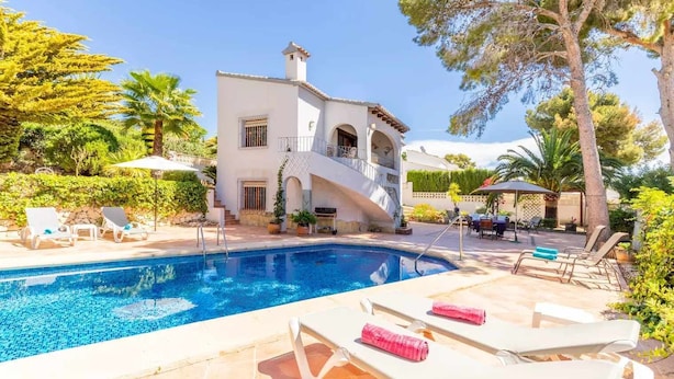 A pool area with lounge chairs, a white building with a balcony, and surrounding greenery. - VILLA FELIZ, beach, pool, wifi, a/a, 10 pax (Moravit)